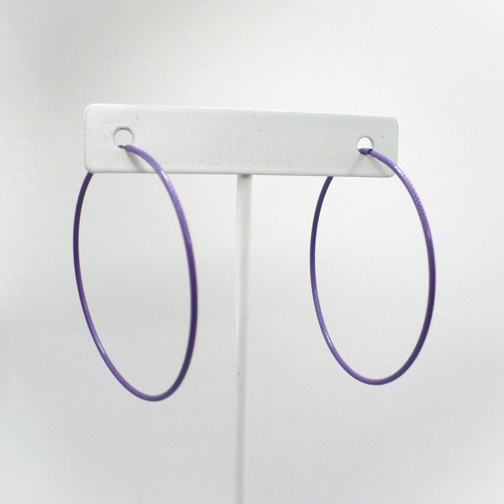 Front-facing view of the 1980s vintage orchid purple pop art Memphis style 2-inch hoop earrings hanging on a white T-bar jewelry display stand against a neutral background.
