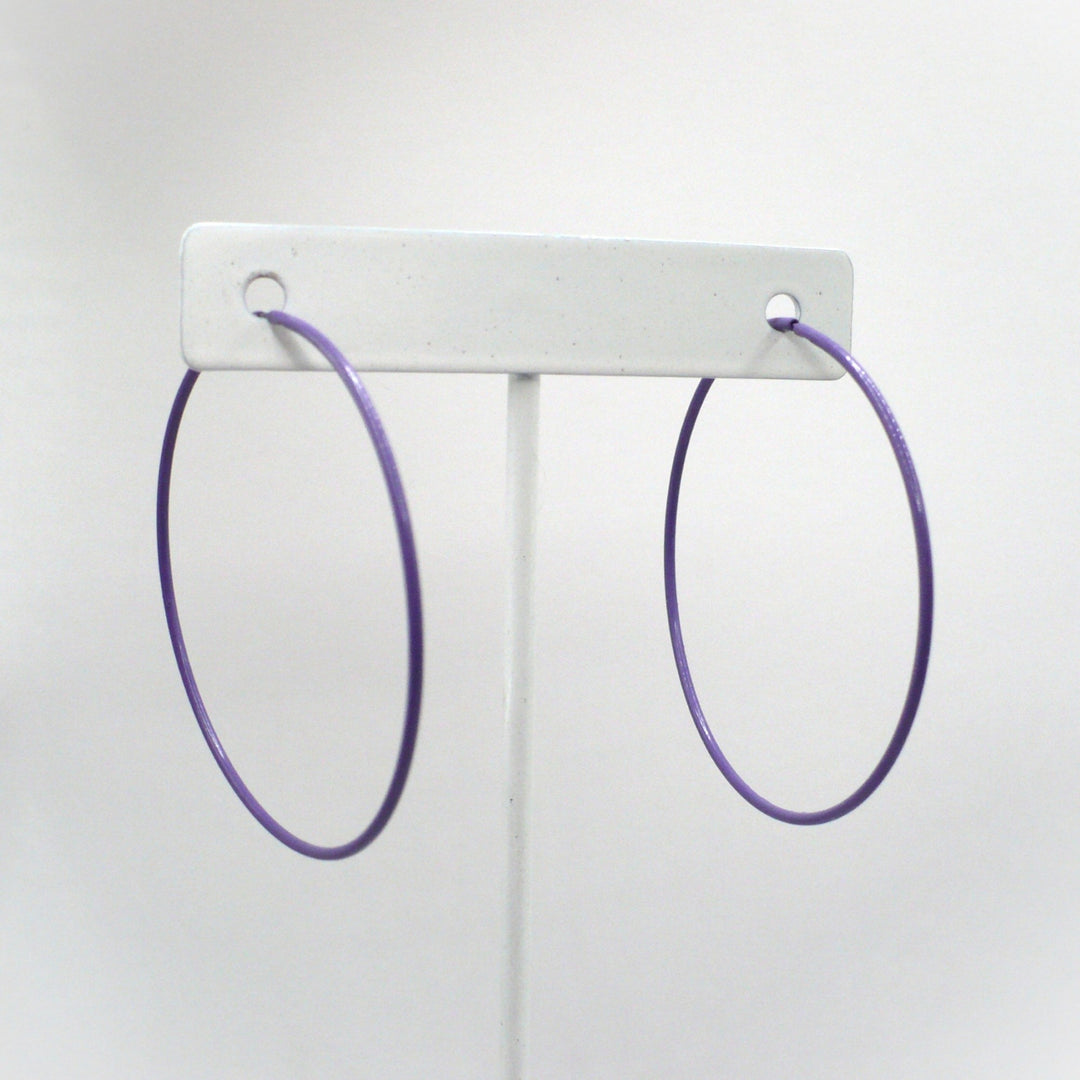 Front-facing view of the 1980s vintage orchid purple pop art Memphis style 2-inch hoop earrings hanging on a white T-bar jewelry display stand against a neutral background.