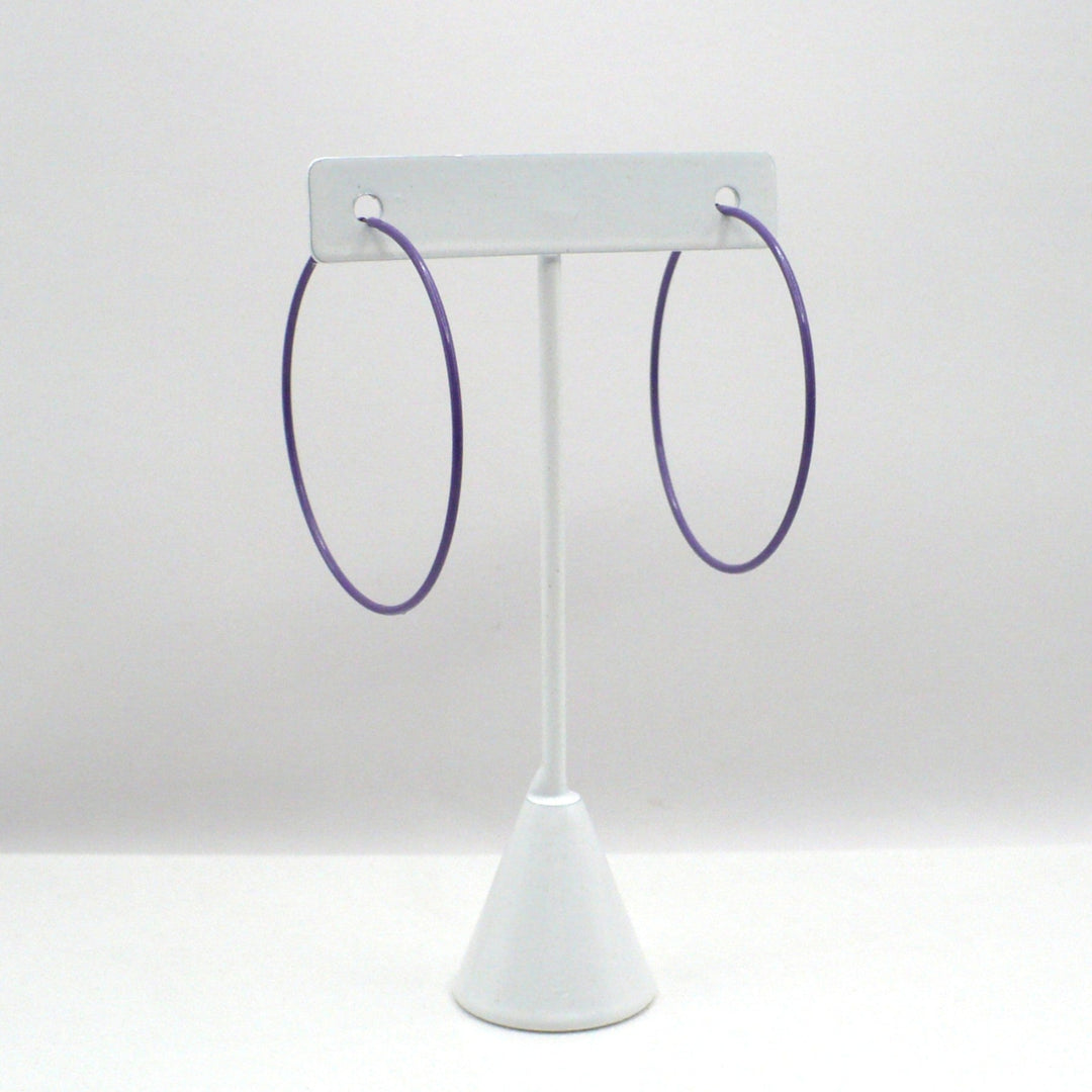 Front-facing view of the 1980s vintage orchid purple pop art Memphis style 2-inch hoop earrings hanging on a white T-bar jewelry display stand against a neutral background.