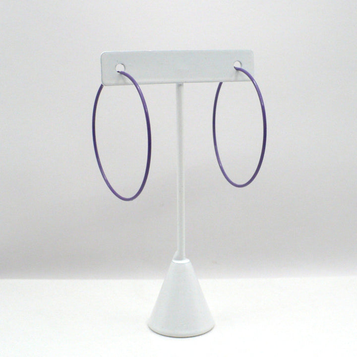 Front-facing view of the 1980s vintage orchid purple pop art Memphis style 2-inch hoop earrings hanging on a white T-bar jewelry display stand against a neutral background.