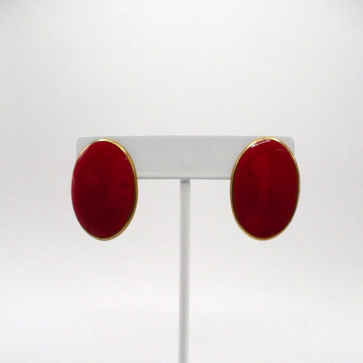 1980s vintage lipstick-red oval statement earrings with gold-tone outlines displayed on a white T-bar stand.
