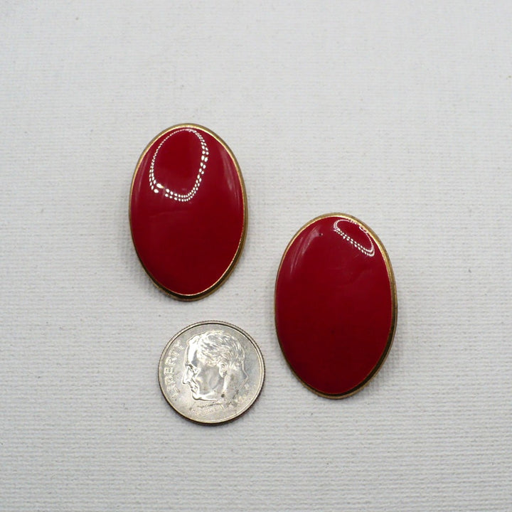 1980s vintage lipstick-red oval statement earrings with gold-tone outlines displayed on a white T-bar stand, on flat surface next to a dime for scale.