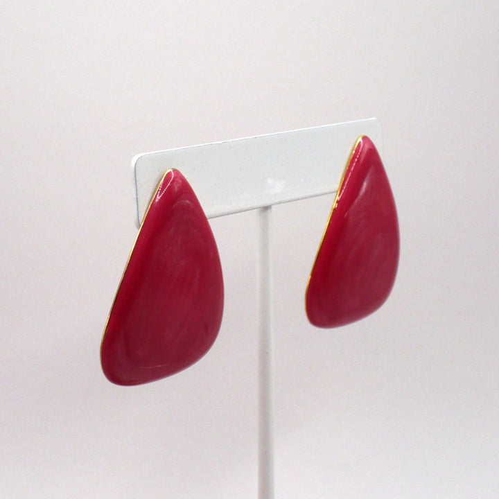 1980s vintage watermelon-pink marbled Lucite triangle statement earrings displayed on a white stand, shown at a slight angle.
