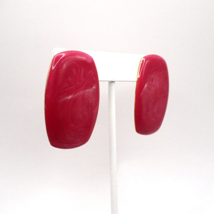 Close-up of 1980s vintage watermelon-pink marbled Lucite barrel earrings showing swirling mica detail.
