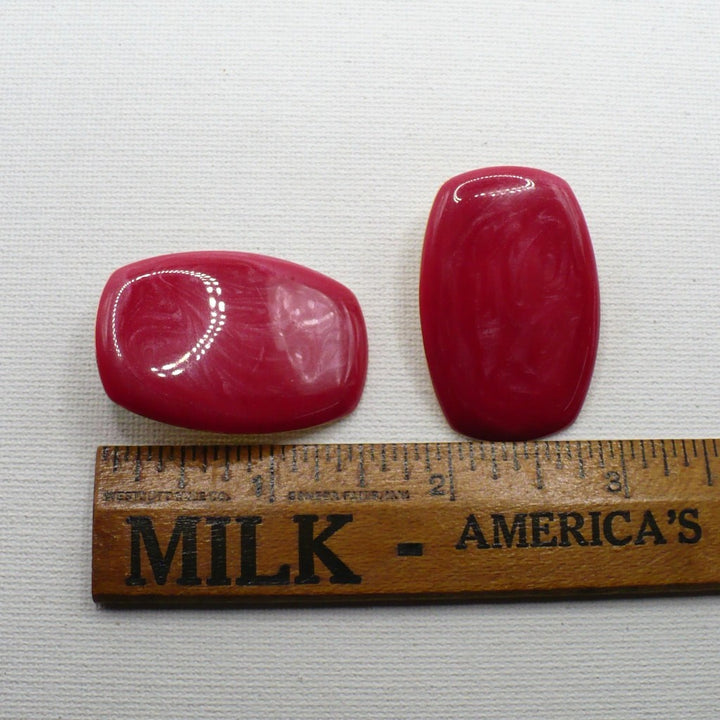 Close-up of 1980s vintage watermelon-pink marbled Lucite barrel earrings on flat surface, next to ruler for scale.