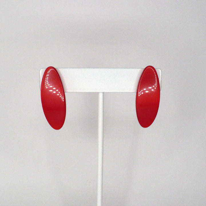 Pair of vintage 1980s New Wave watermelon red Lucite oval statement earrings displayed on a white stand.