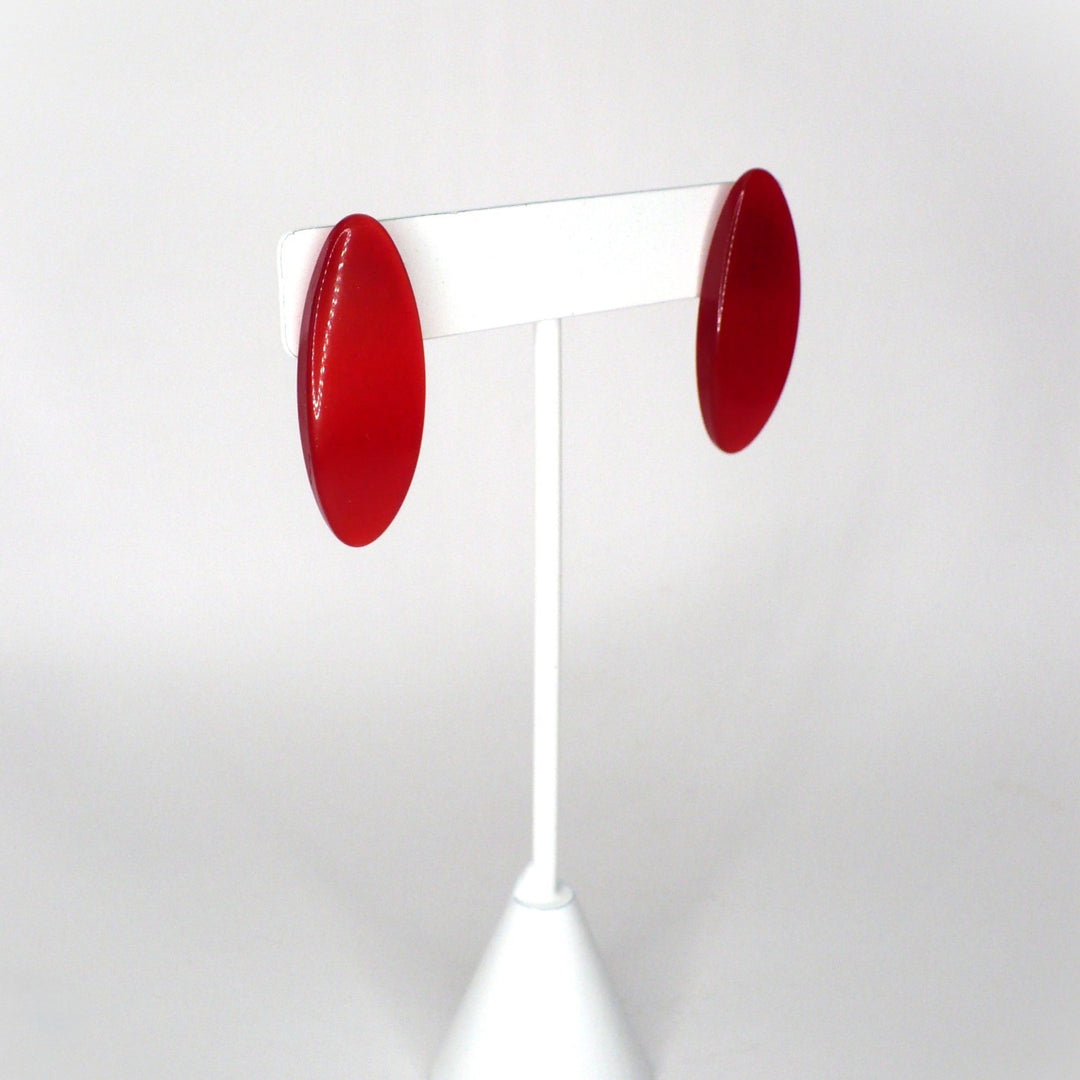Retro red glossy acrylic oval stud earrings from the 1980s against a neutral background, angle view.