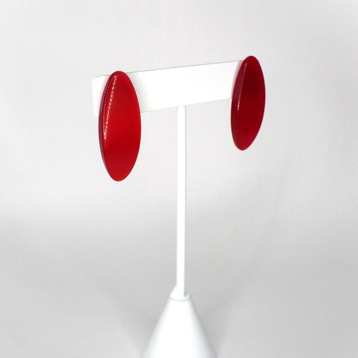 Retro red glossy acrylic oval stud earrings from the 1980s against a neutral background, angle view.