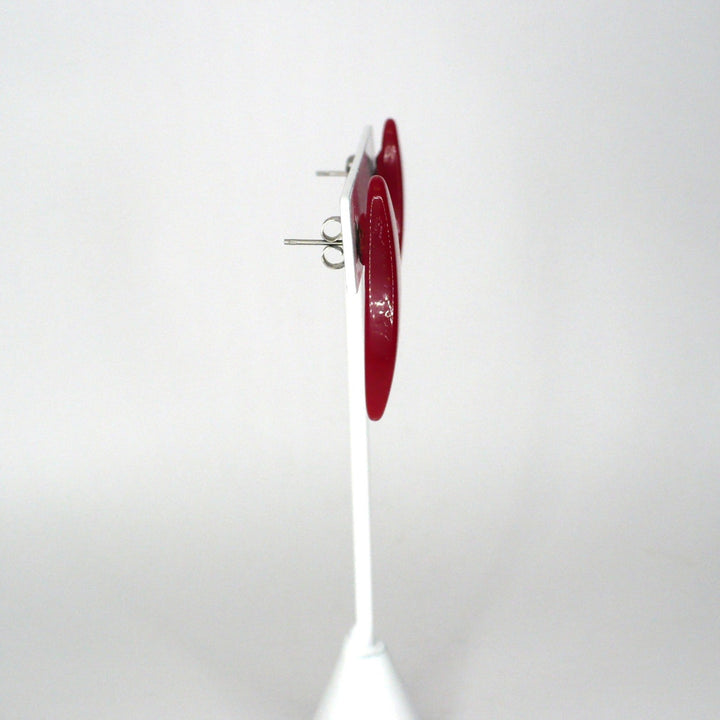 Side profile view of a vintage 1980s watermelon red Lucite oval statement earring on a display stand.