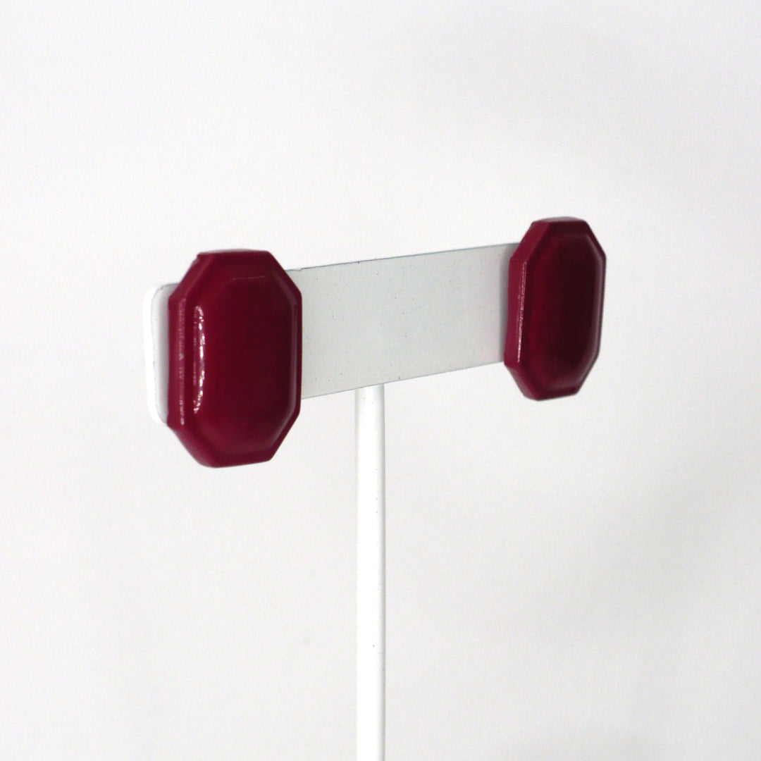 1980s vintage burgundy maroon emerald-cut enamel geometric button earrings on a white display stand, angled view.