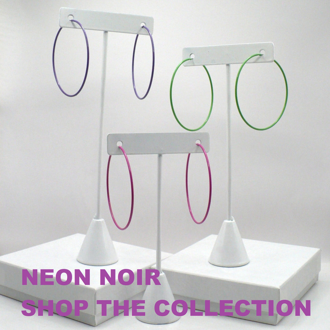 1980s pop art Memphis style hoop earrings in purple, green, and pink displayed on three white T-stand holders above a neon noir collection graphic.