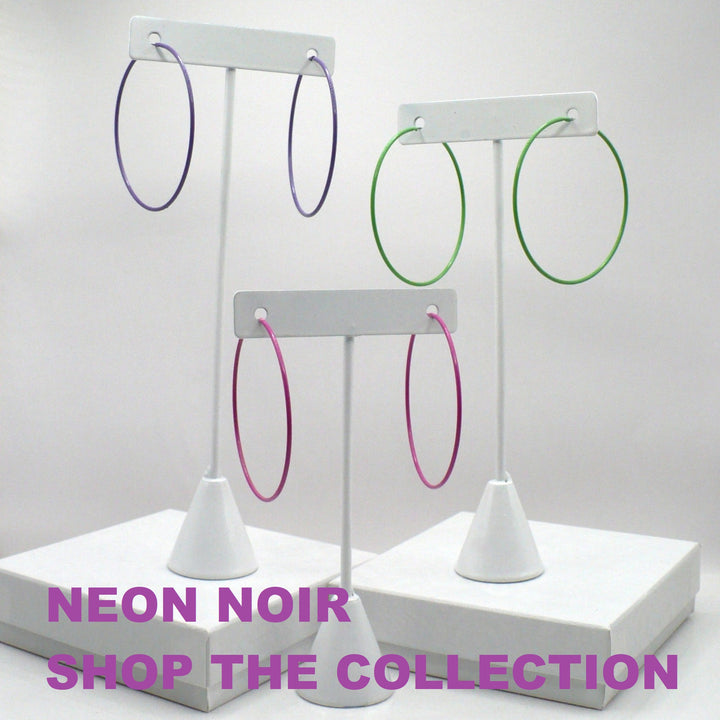 1980s pop art Memphis style hoop earrings in purple, green, and pink displayed on three white T-stand holders above a neon noir collection graphic.