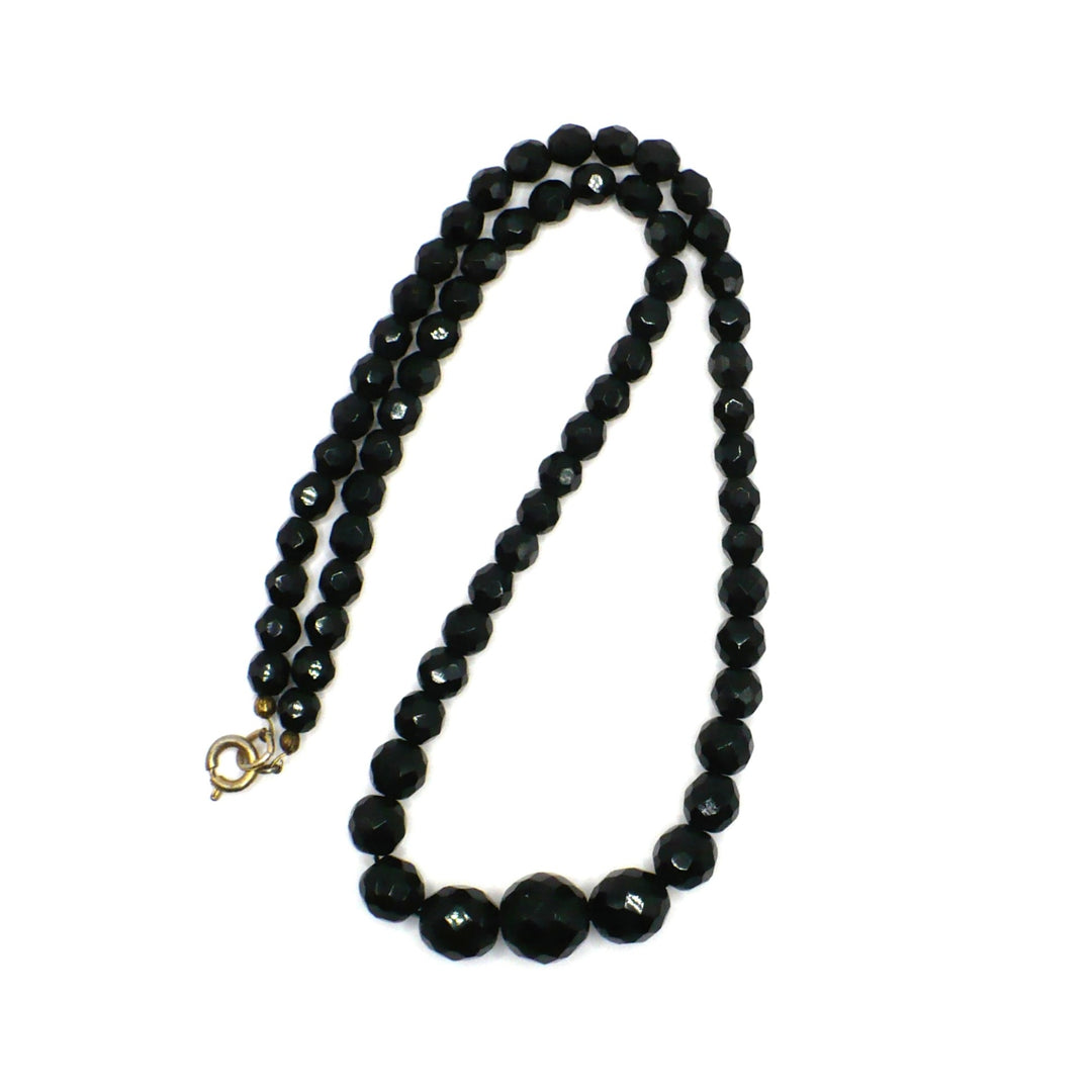 Vintage 1950s black faceted glass beaded necklace arranged in a folded double-strand loop against a white background.
