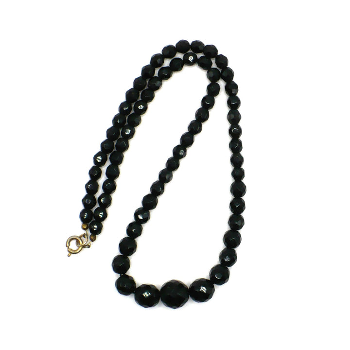 Vintage 1950s black faceted glass beaded necklace arranged in a folded double-strand loop against a white background.