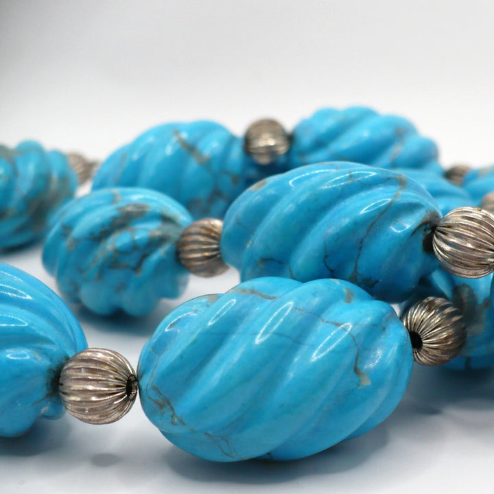 Close-up view of carved blue Howlite beads showing the detailed carving texture and round silver beads.
