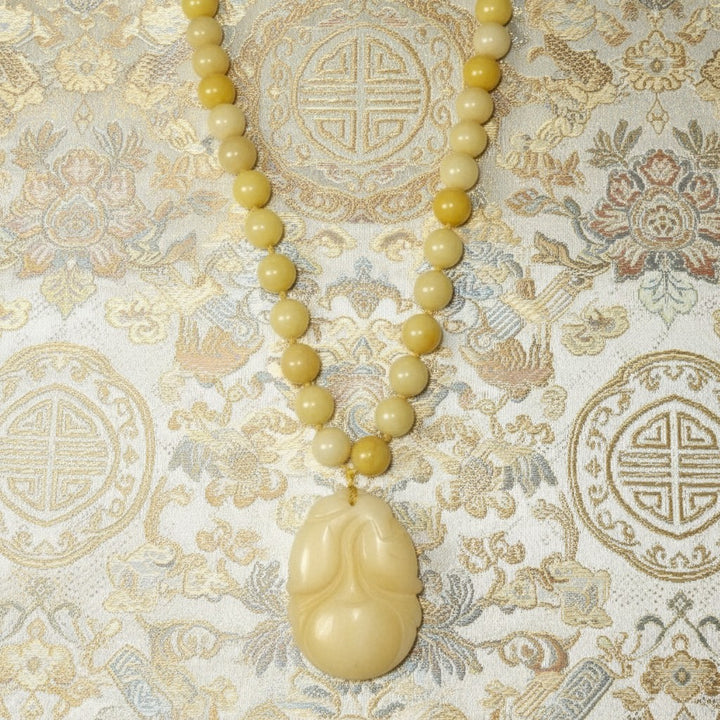 Vintage 1970s yellow nephrite jade beaded necklace featuring a hand-carved persimmon pendant laid flat against an ornate traditional golden silk background.