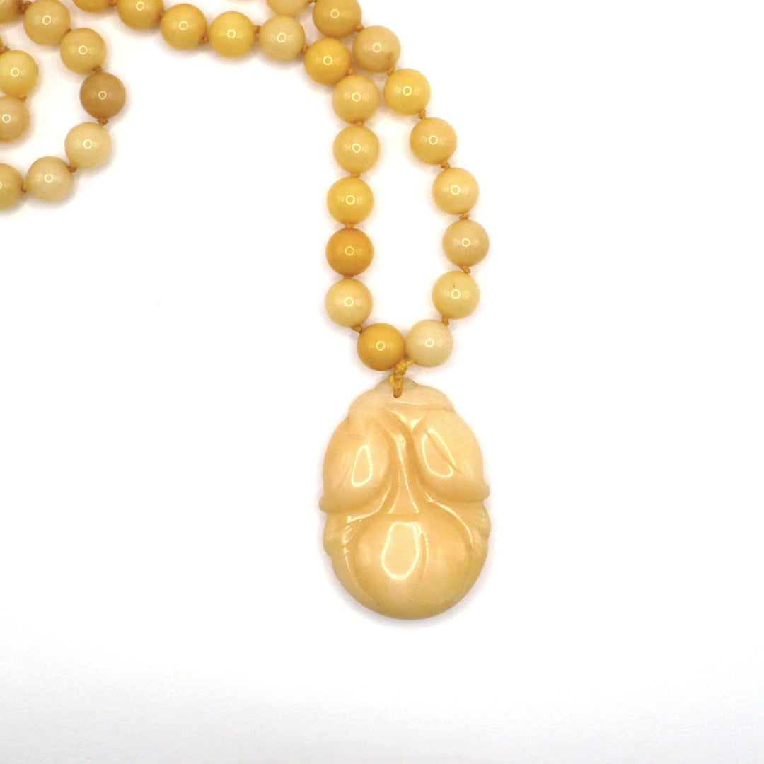 Close-up product shot of the vintage 1970s yellow nephrite jade beaded necklace focusing on the carved persimmon pendant.