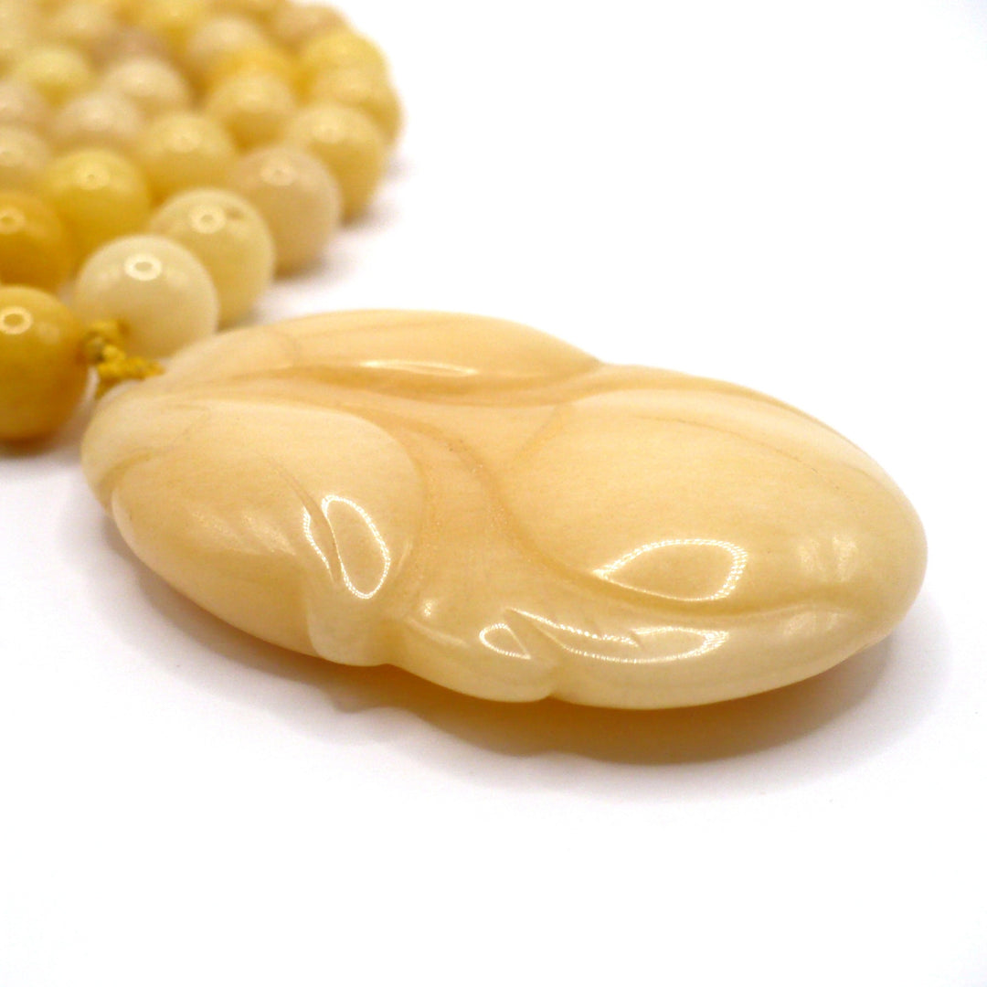Macro shot of the carved yellow nephrite jade persimmon pendant, highlighting the smooth texture and warm tones of the vintage 1970s Chinese export necklace.