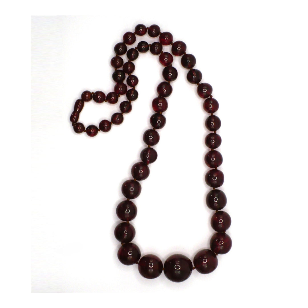 1920s antique cherry amber beaded necklace laid out in a loop, showing graduated deep red-brown Baltic amber beads.