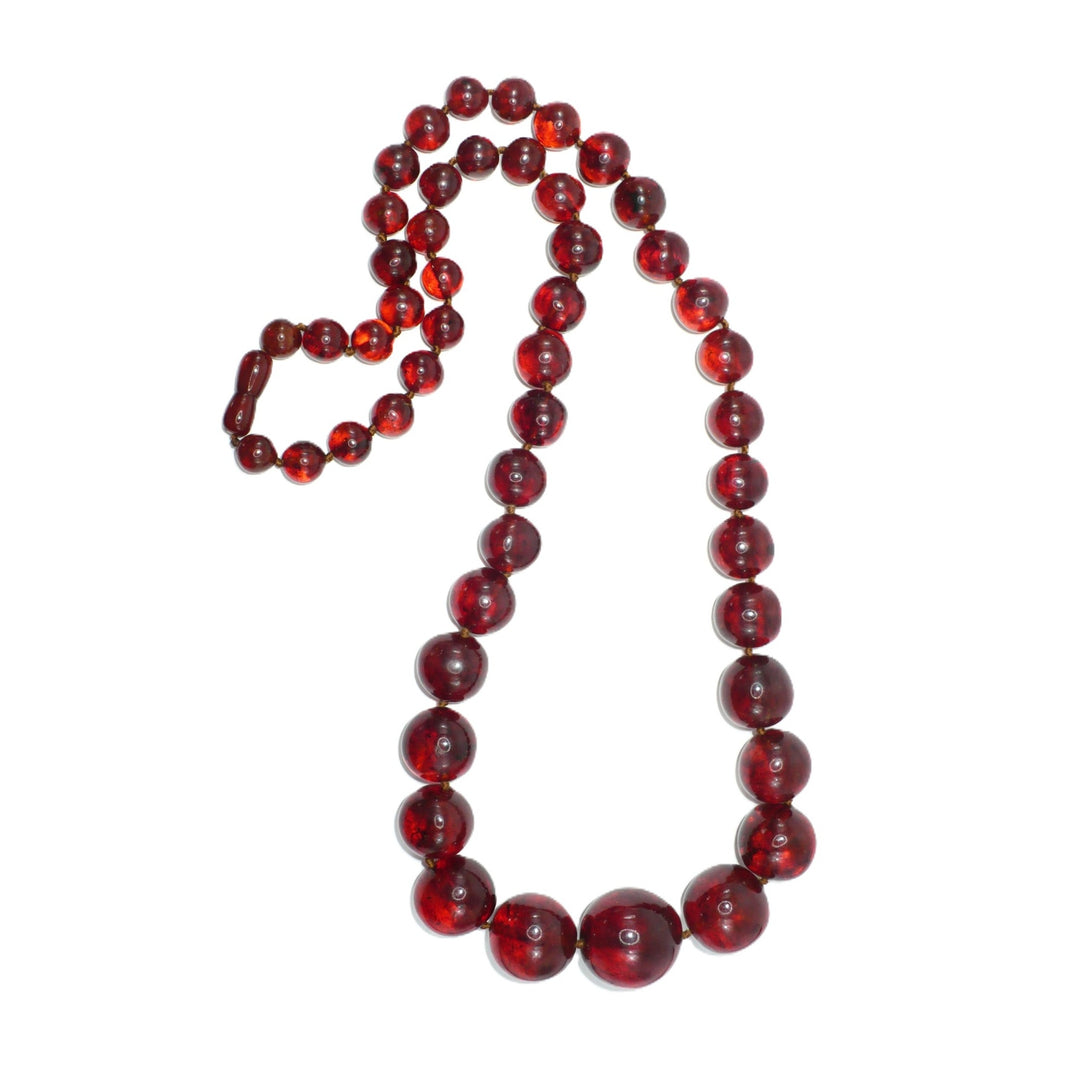 1920s antique cherry amber beaded necklace laid out in a loop, showing graduated deep red-brown Baltic amber beads, taken with a flash.