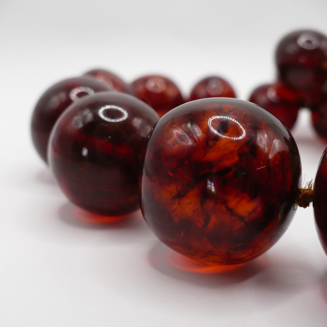 Macro close-up view of large, graduated antique cherry amber beads showing natural organic texture and deep oxidation.