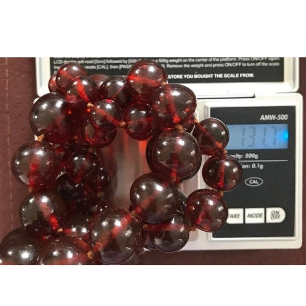 1920s antique cherry amber beaded necklace on a digital scale showing a weight of 131.7 grams.