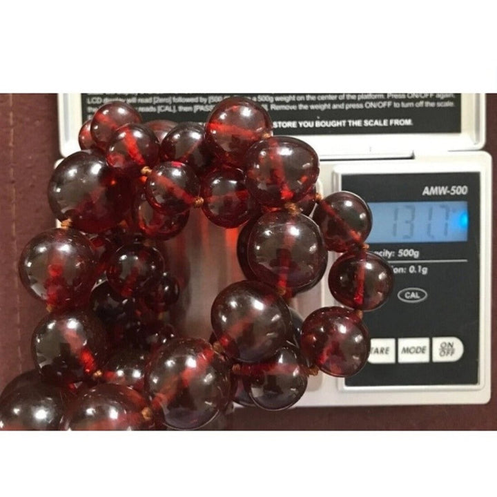 1920s antique cherry amber beaded necklace on a digital scale showing a weight of 131.7 grams.