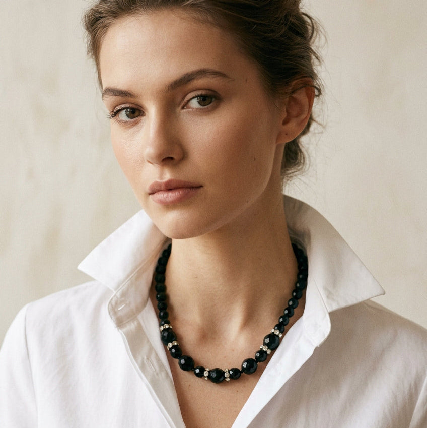 Model wearing the 1950s vintage graduated black faceted glass beaded necklace with rhinestone rondelles against a white collared shirt.