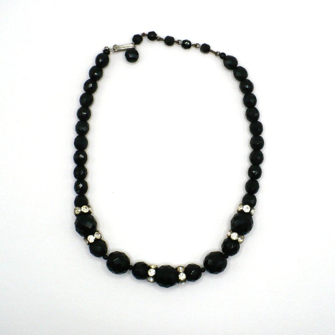1950s vintage graduated black faceted glass beaded necklace with rhinestone rondelles displayed on a white background.