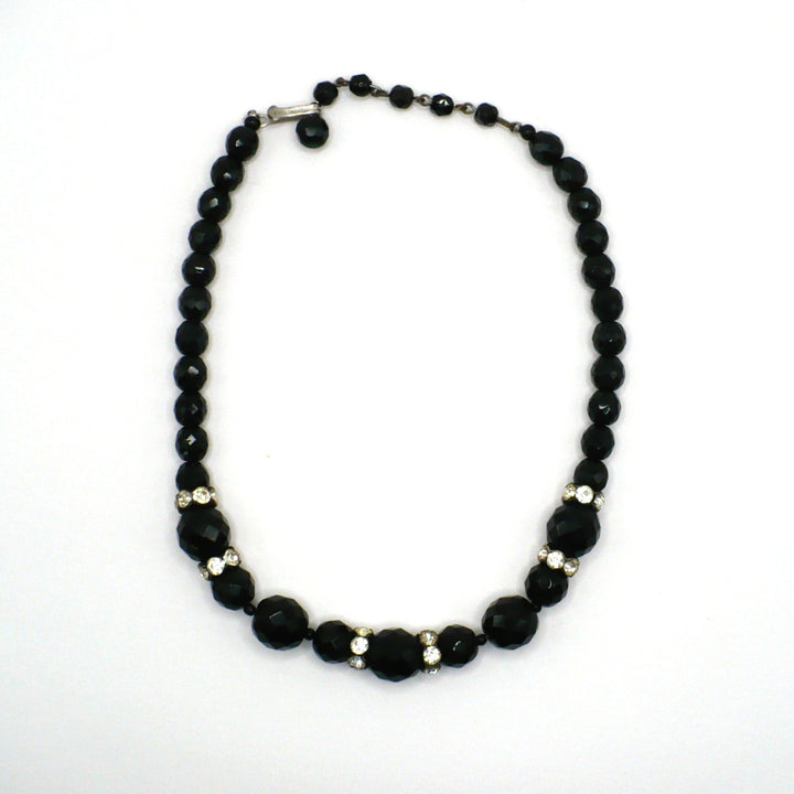 1950s vintage graduated black faceted glass beaded necklace with rhinestone rondelles displayed on a white background.