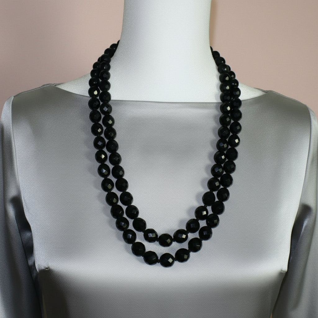 1950s vintage multi-strand black faceted glass bead necklace with a gold-toned ornamental box clasp on a gray silk shirt.