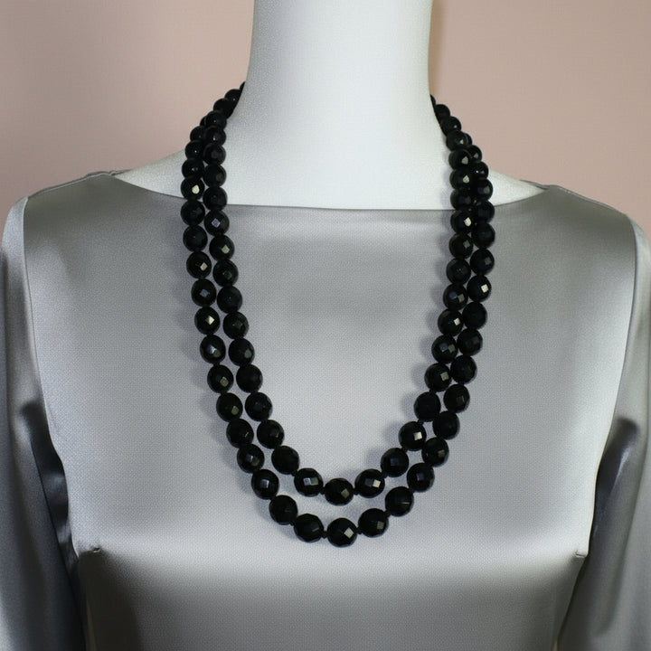 1950s vintage multi-strand black faceted glass bead necklace with a gold-toned ornamental box clasp on a gray silk shirt.