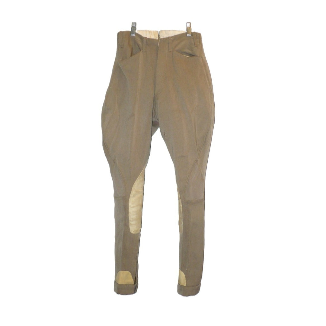 A pair of children's vintage equestrian breeches in a muted taupe-brown color, featuring light beige leather knee patches and matching ankle patches, shown hanging against a plain white background, fronts.