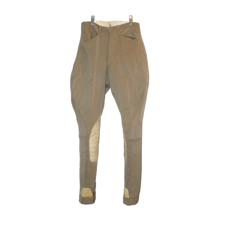 A pair of children's vintage equestrian breeches in a muted taupe-brown color, featuring light beige leather knee patches and matching ankle patches, shown hanging against a plain white background, fronts.