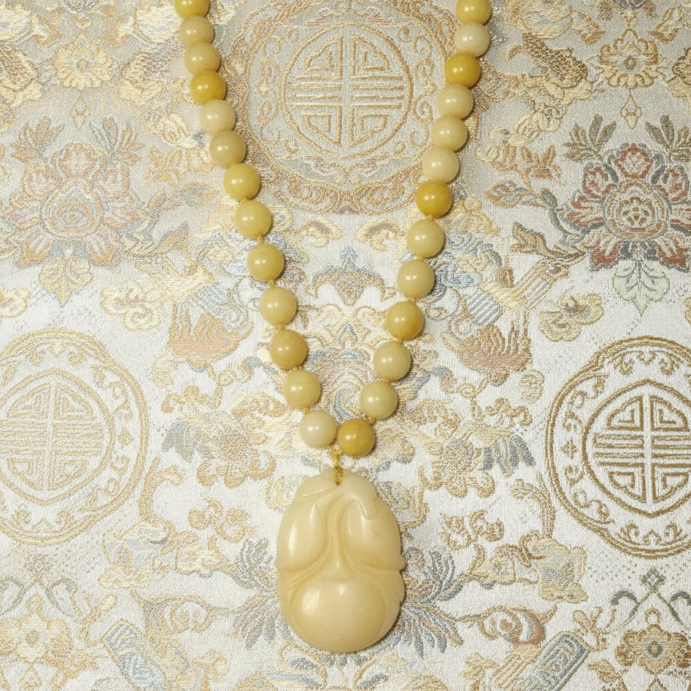 Shows close up of Post Mao Vintage Yellow Jade Necklace Hand-Carved Persimmon Pendant with fabric background.
