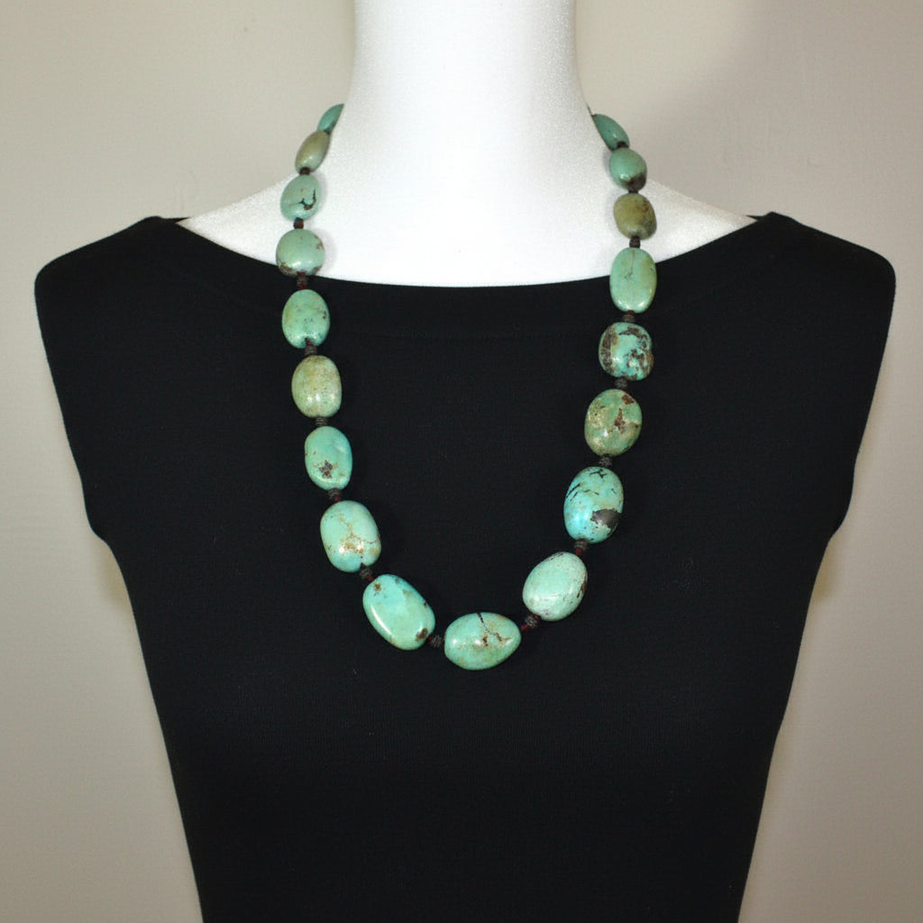 Turquoise beaded necklace on a mannequin with a black dress against a neutral background