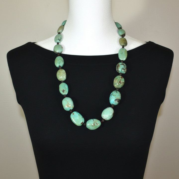 Turquoise beaded necklace on a mannequin with a black dress against a neutral background