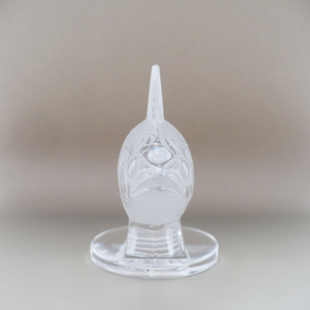 A frosted crystal fish sculpture, Perche Bouchon de Radiateur: Perch Car Mascot, displayed on a clear glass stand against a neutral beige background, facing forward.