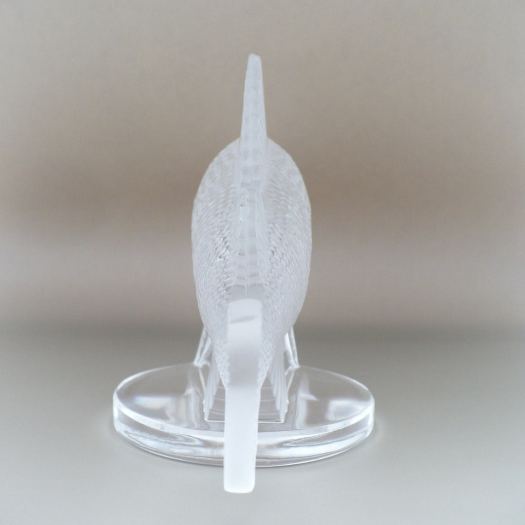 A frosted crystal fish sculpture, Perche Bouchon de Radiateur: Perch Car Mascot, displayed on a clear glass stand against a neutral beige background, view of back.
