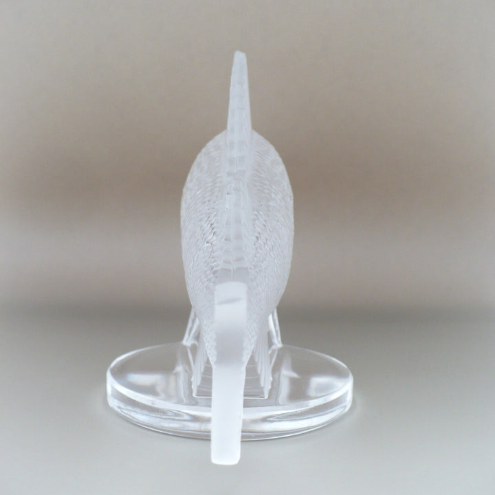 A frosted crystal fish sculpture, Perche Bouchon de Radiateur: Perch Car Mascot, displayed on a clear glass stand against a neutral beige background, view of back.
