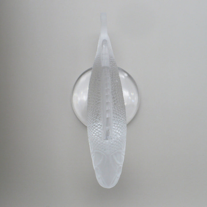 A frosted crystal fish sculpture, Perche Bouchon de Radiateur: Perch Car Mascot, displayed on a clear glass stand against a neutral beige background, view from above.