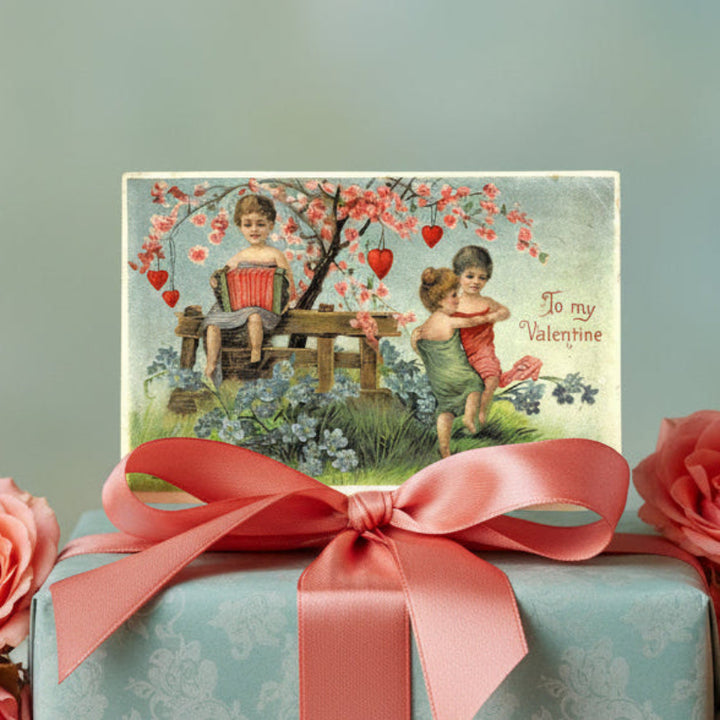 1910 Young Love Embossed Vintage Valentine Postcard and a pink ribbon on a gift box.