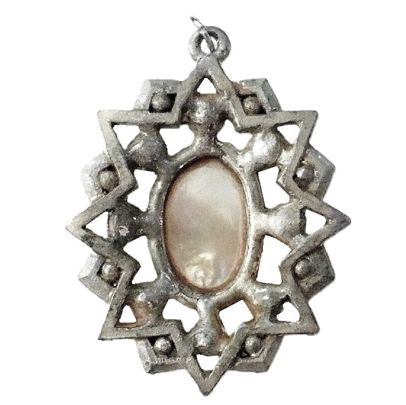 A vintage 1950s pendant featuring a cross with faceted Aurora Borealis stones and simulated pearls, set against an oval mother-of-pearl center, with intricate eloxal metalwork. Back view.