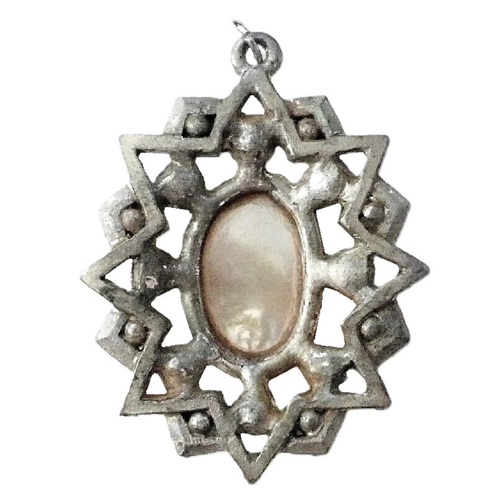 A vintage 1950s pendant featuring a cross with faceted Aurora Borealis stones and simulated pearls, set against an oval mother-of-pearl center, with intricate eloxal metalwork. Back view.