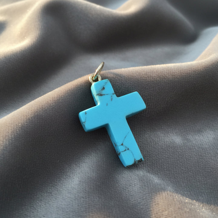 Blue Howlite cross pendant on gray background.