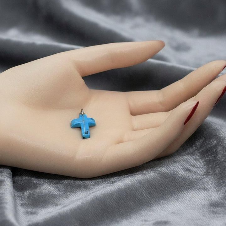 Blue Howlite cross pendant on palm of hand on gray background.
