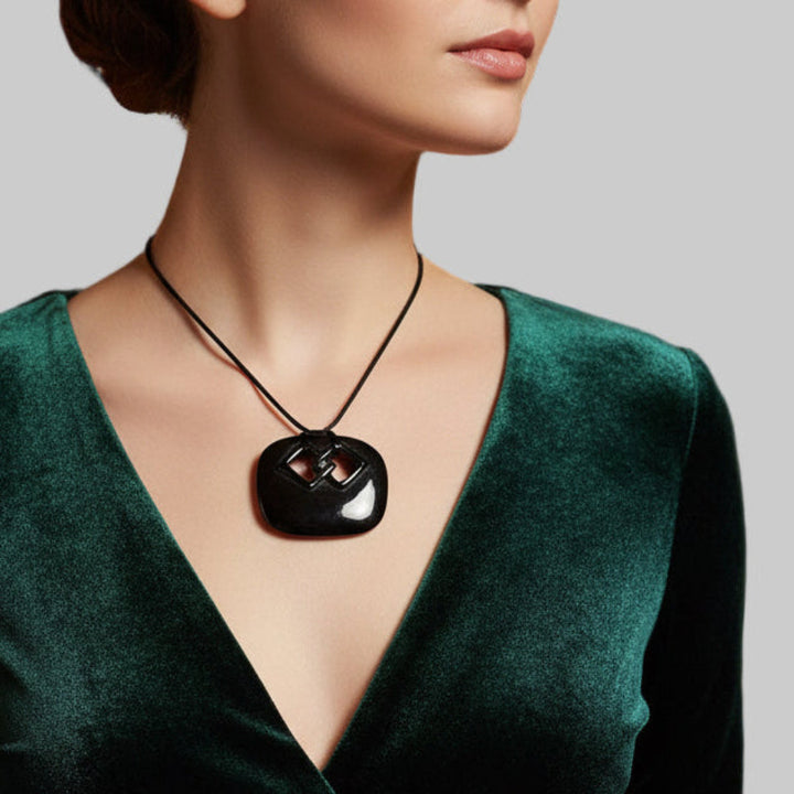 Woman wearing a green velvet top with a black pendant necklace on a neutral background