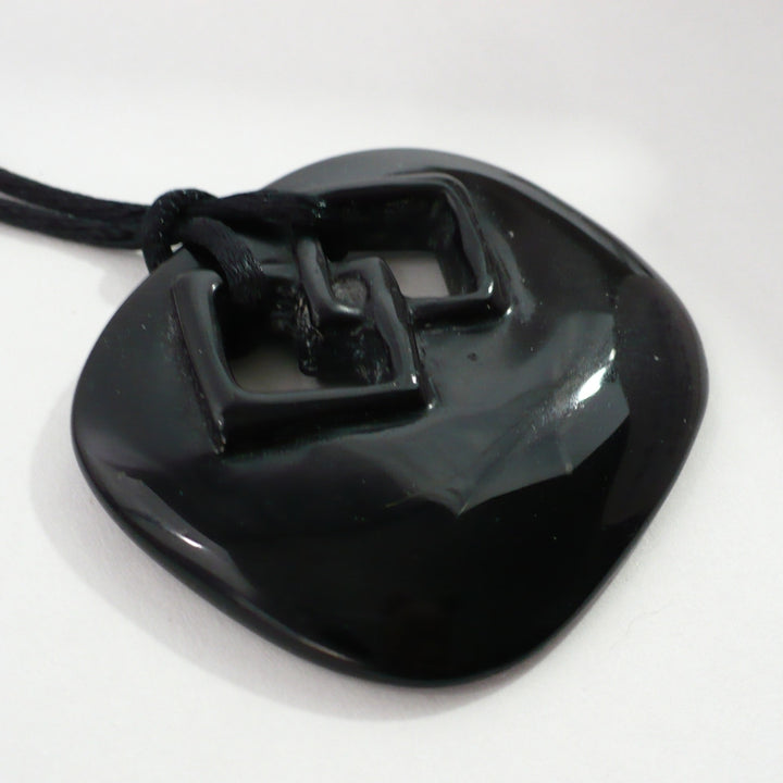 Angled close-up view showing the raised relief texture of the vintage black ceramic endless knot pendant.