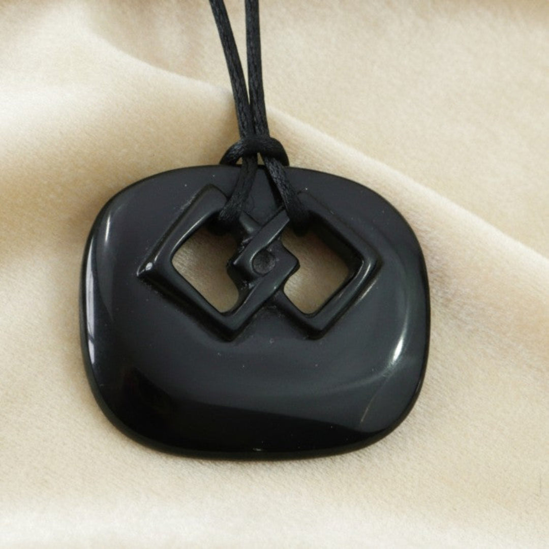 1980s handmade black ceramic endless knot pendant with black satin cord on a cream background.