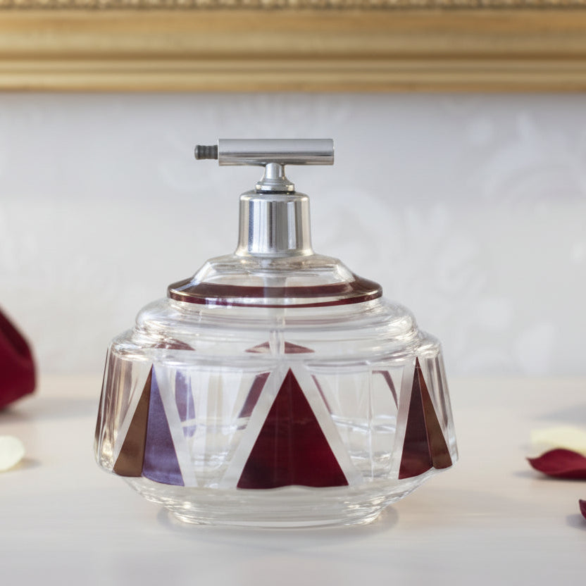 1930s Art Deco Palda Red Perfume Atomizer on a surface with rose petals, against a decorative mirror.